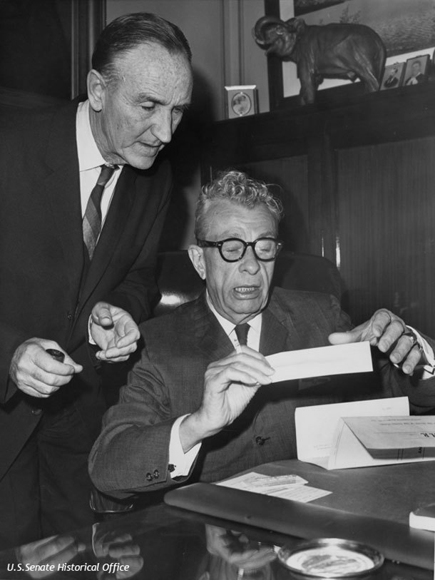 Senator Mike Mansfield standing behind Senator Everett Dirksen who is typing a document.
