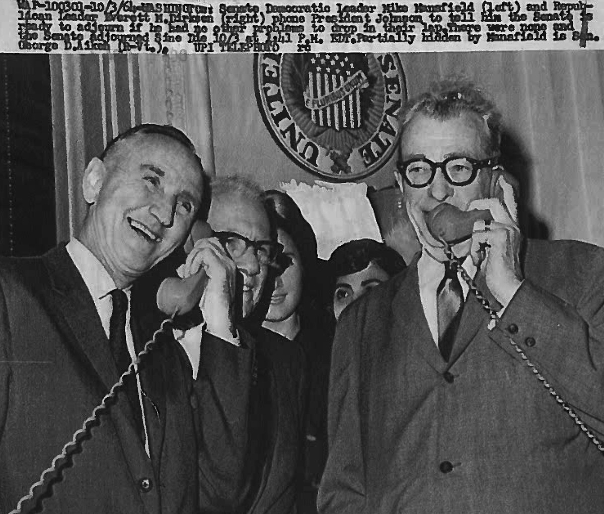 Senators Mike Mansfield and Everett Dirksen smiling and each speaking into a telephone.