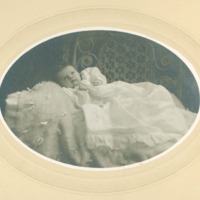 Baby in christening gown, on fluffy blanket laid on ornate cane chair